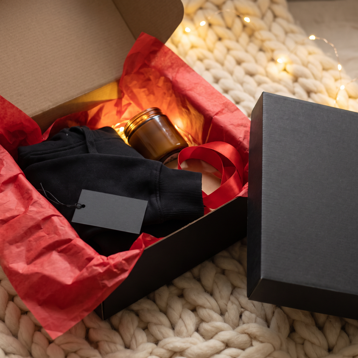 Love Cork Screw Mystery Cozy Box, a black gift box with red tissue paper and a surprise hoodie and candle inside