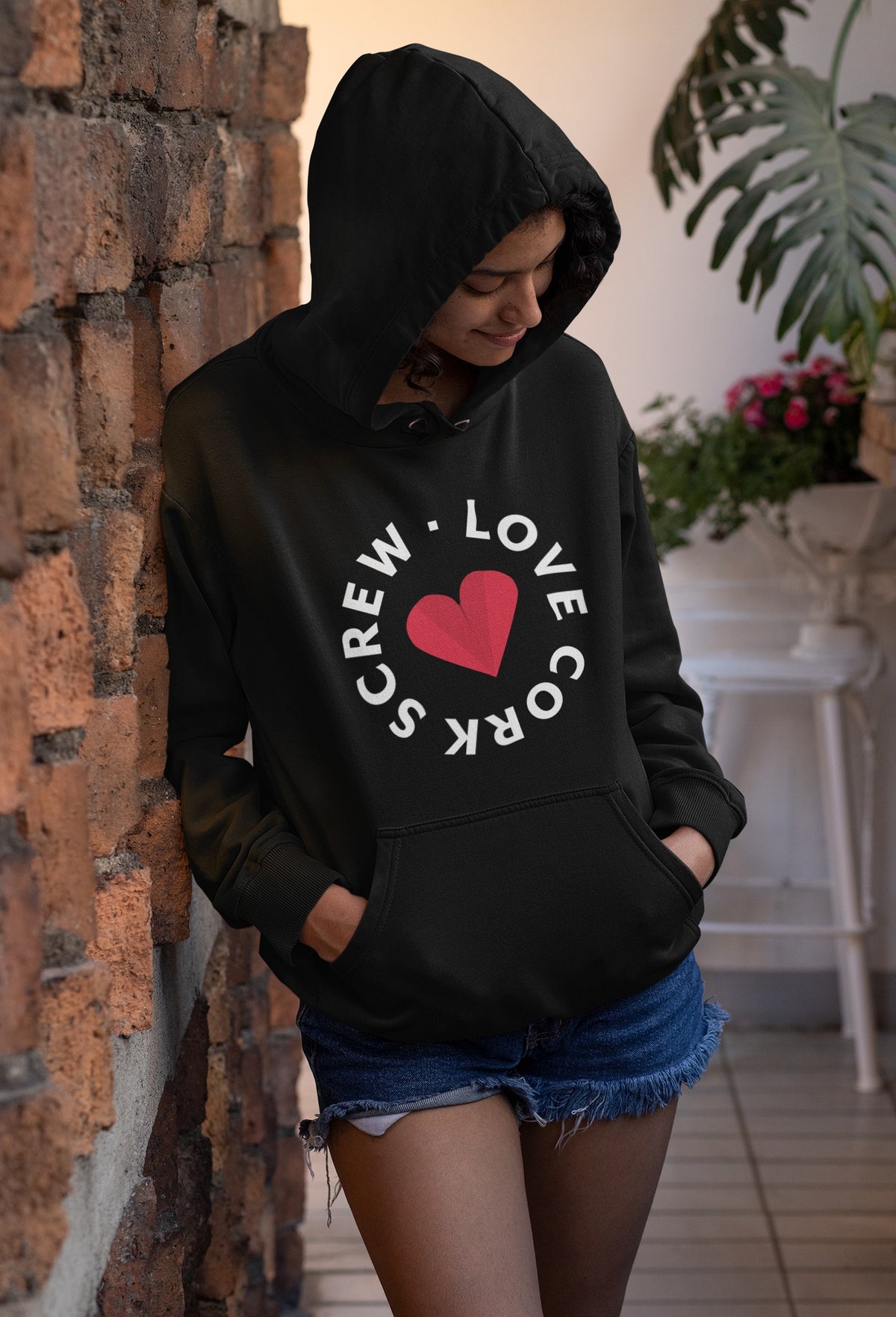 Woman wearing the black Love Cork Screw logo hoodie against a brick wall